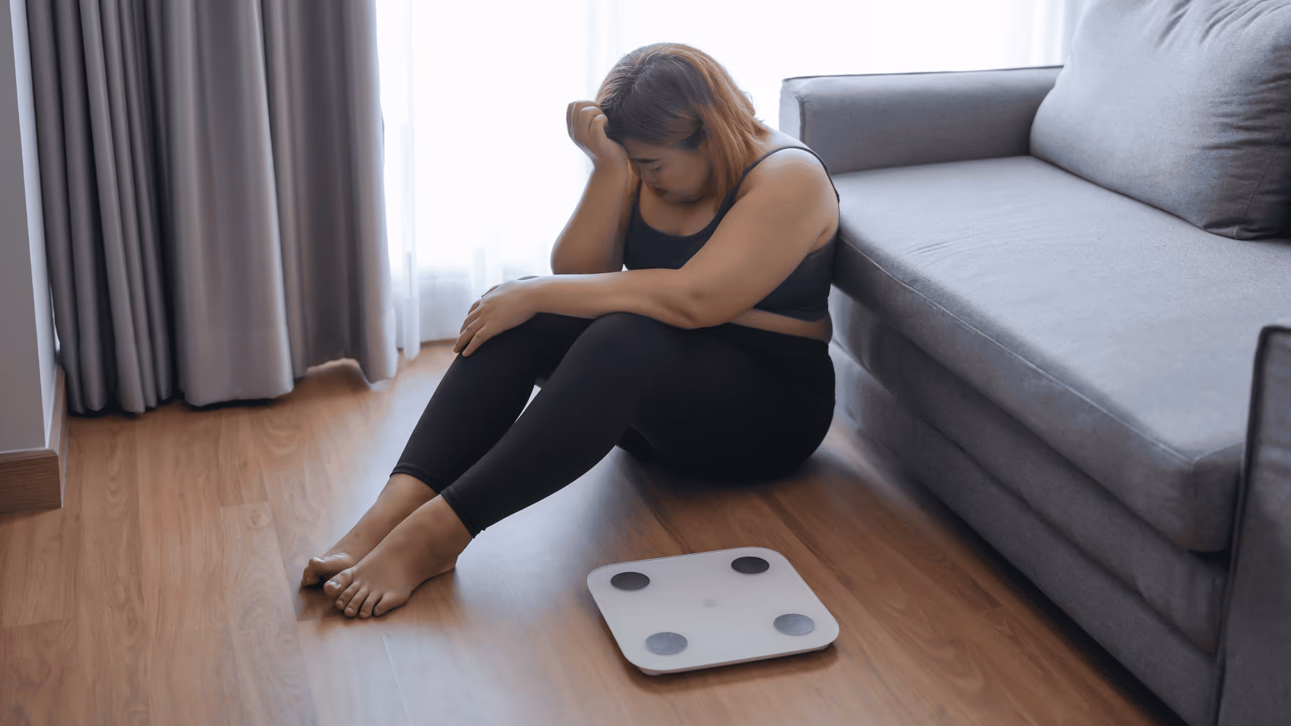 Frau sitzt frustriert neben der Waage, verzweifelt über ihr Gewicht und den Jojo Effekt beim Abnehmen.