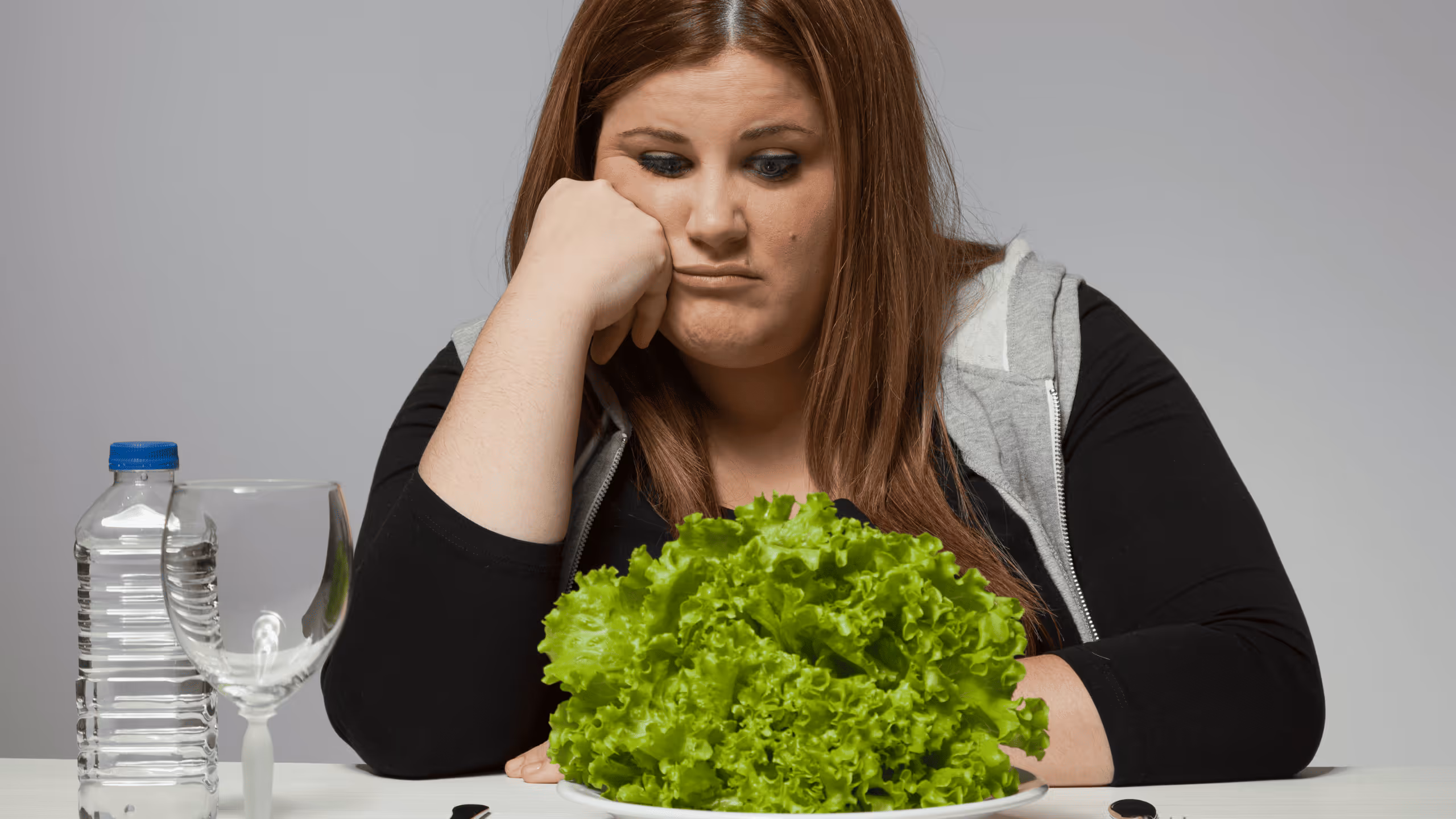 Frau sitzt frustriert vor einem Teller Salat – Diätfrust und falscher Ansatz beim Abnehmen führen oft zum Jojo Effekt.