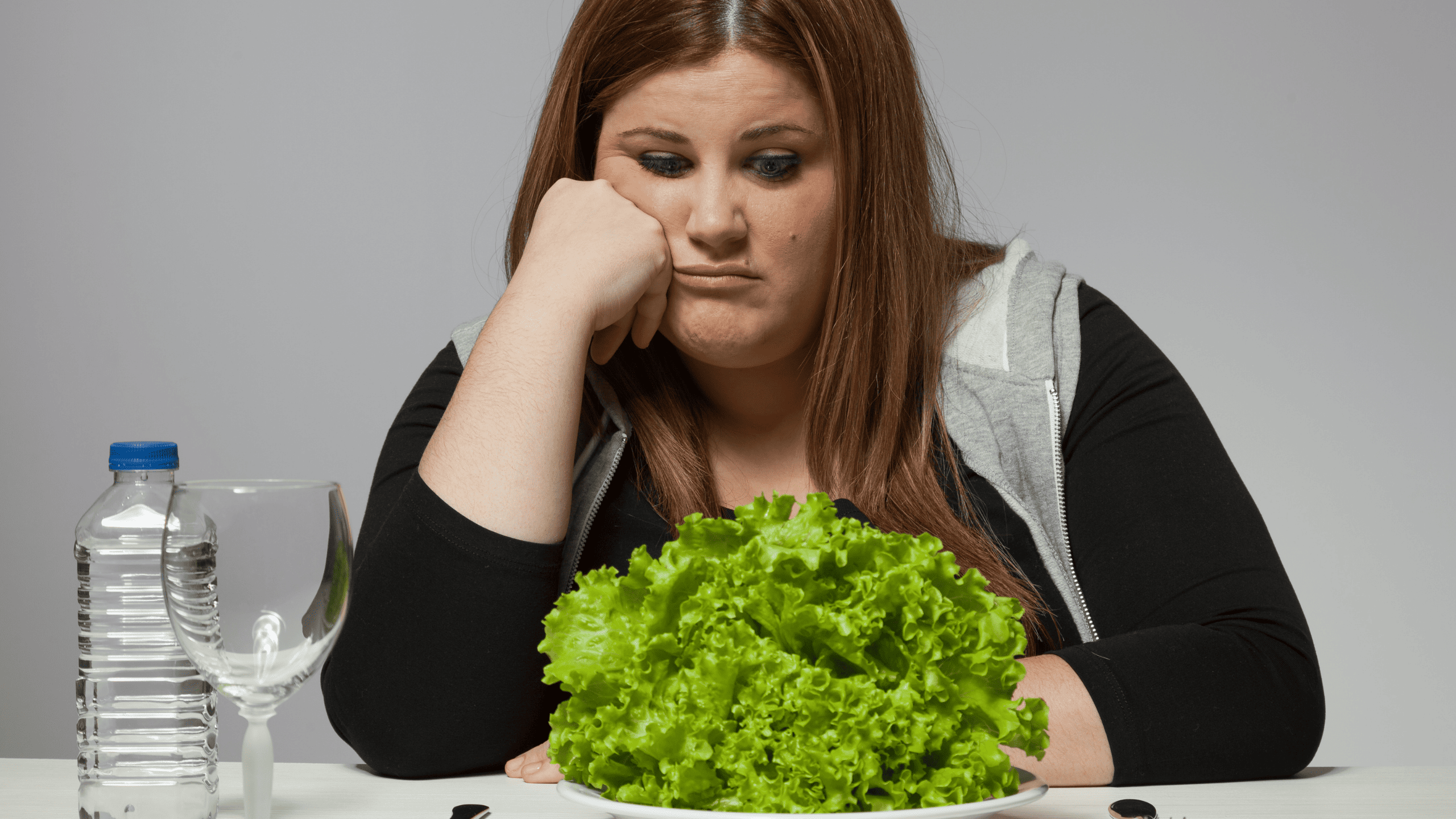 Frau sitzt frustriert vor einem Teller Salat – Diätfrust und falscher Ansatz beim Abnehmen führen oft zum Jojo Effekt.