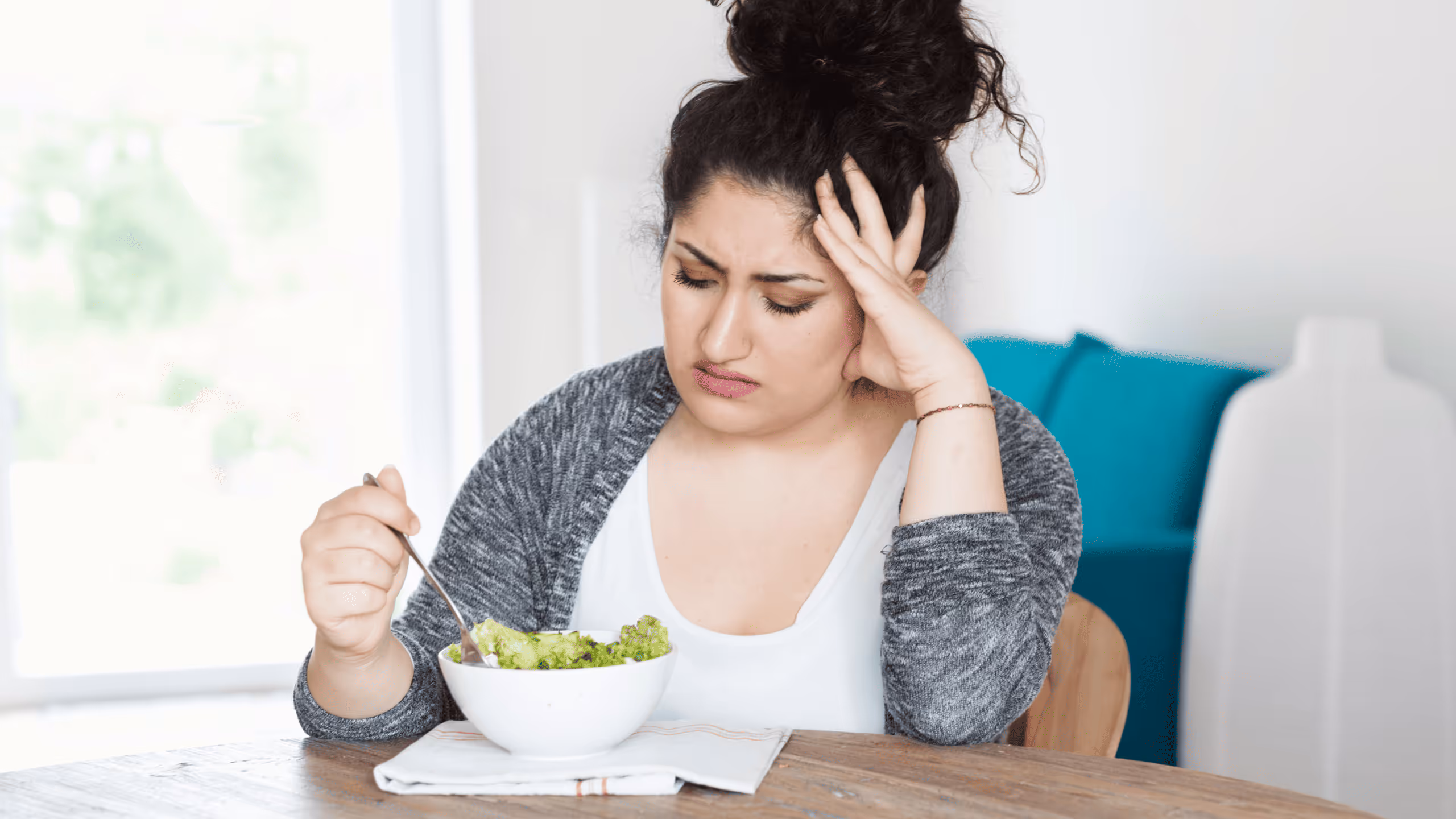 Frau sitzt unzufrieden vor einem kleinen Salatteller – Symbol für zu wenige Mahlzeiten und unzureichende Sättigung.