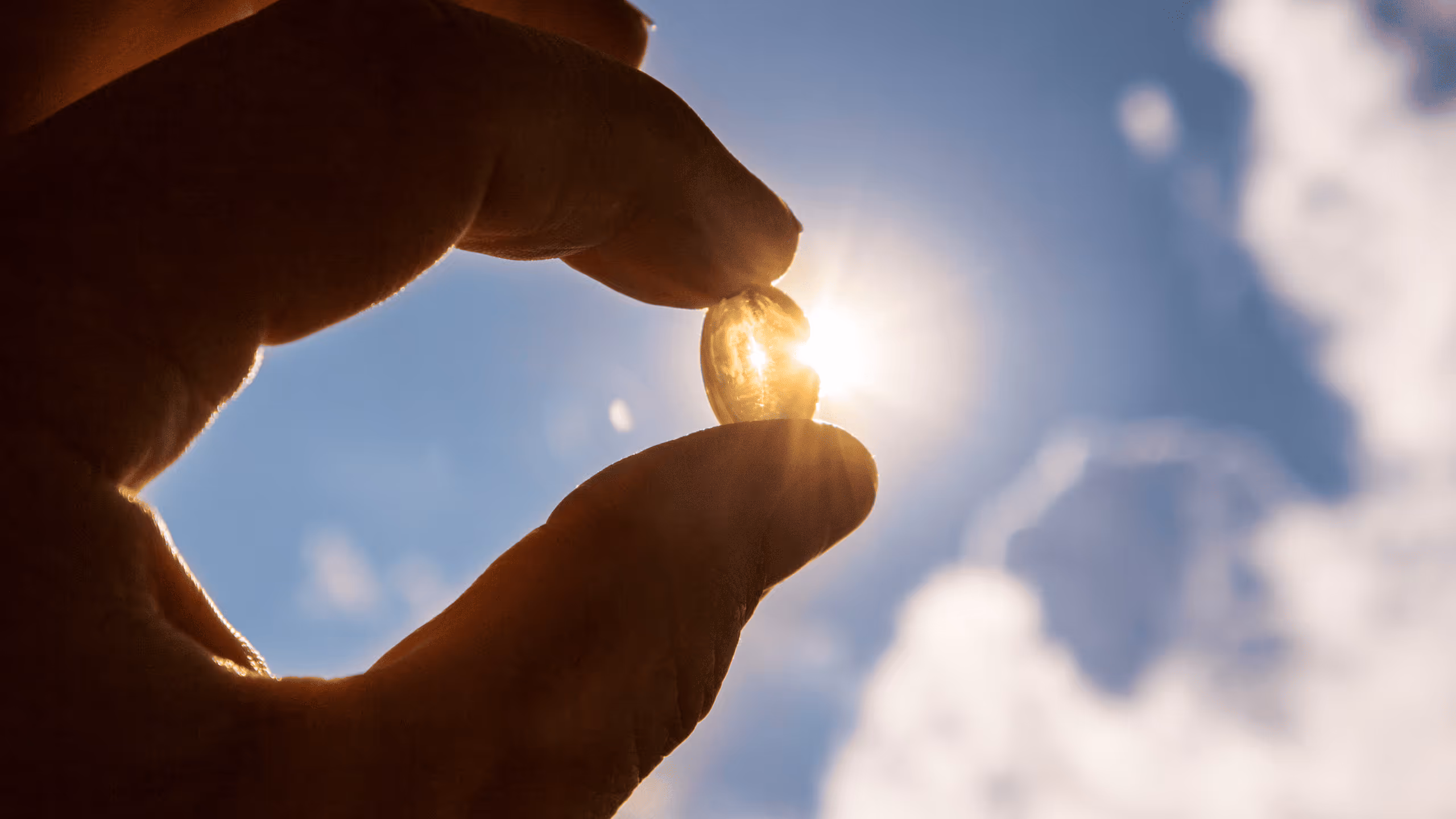 Hand hält eine Vitamin-D-Kapsel ins Sonnenlicht – Symbol für die Wirkung von Nahrungsergänzungsmitteln auf Immunsystem und Energie.