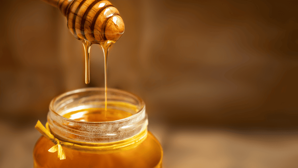 Frischer Honig, der von einem Honiglöffel in ein Glas tropft – Symbol für natürliche Zuckerarten und Honig-Mythen.