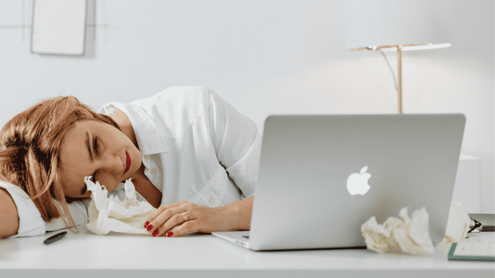 Frau sitzt erschöpft am Schreibtisch und wirkt hormonell belastet – typische Beschwerden unter hormoneller Verhütung.