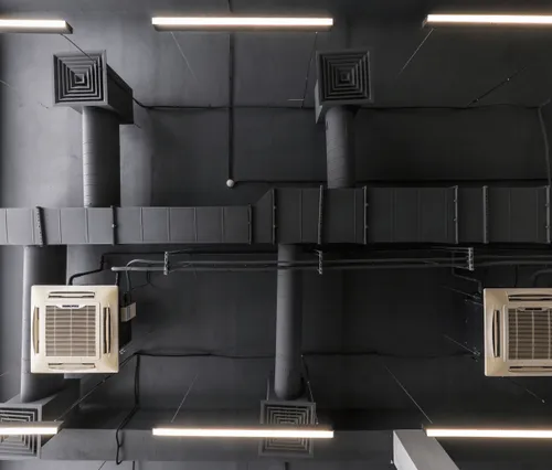 Industrial ceiling with air conditioning units and black ductwork in a modern workspace.