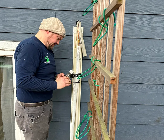 A technician installs outdoor equipment on a wall with green support ties.
