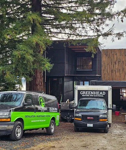 Construction site featuring Greenhead heating and electrical services vans near a modern building under renovation.
