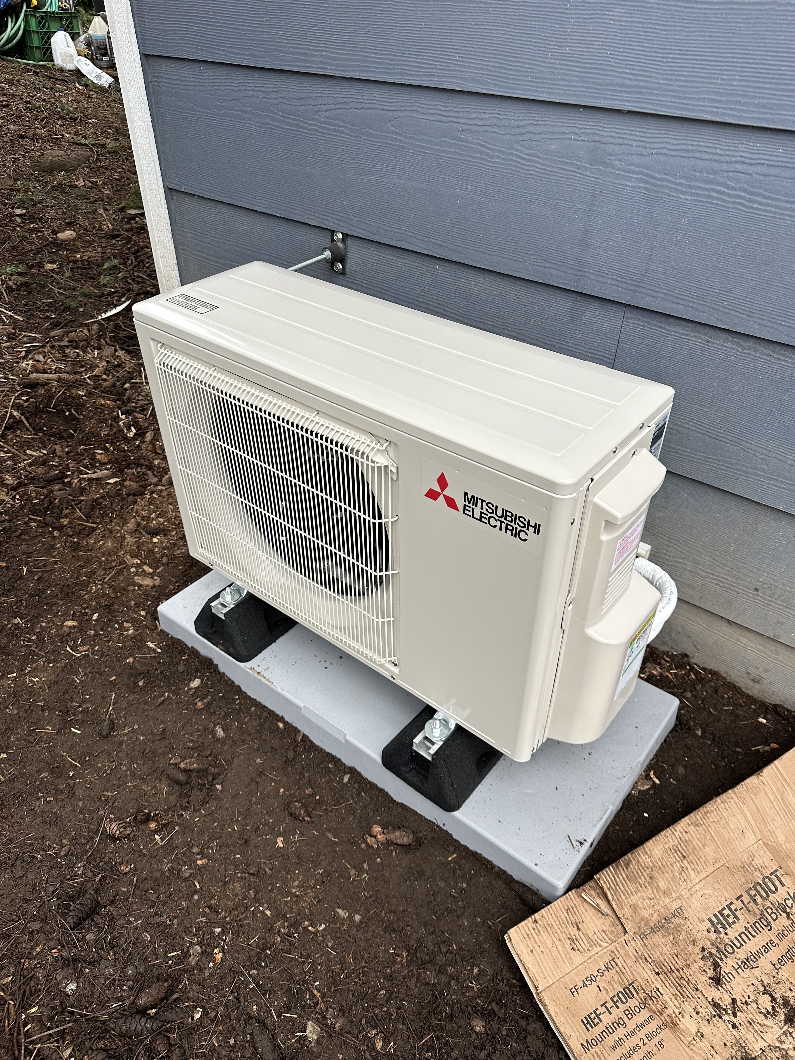 Mitsubishi Electric outdoor unit installed on a concrete pad next to a house.
