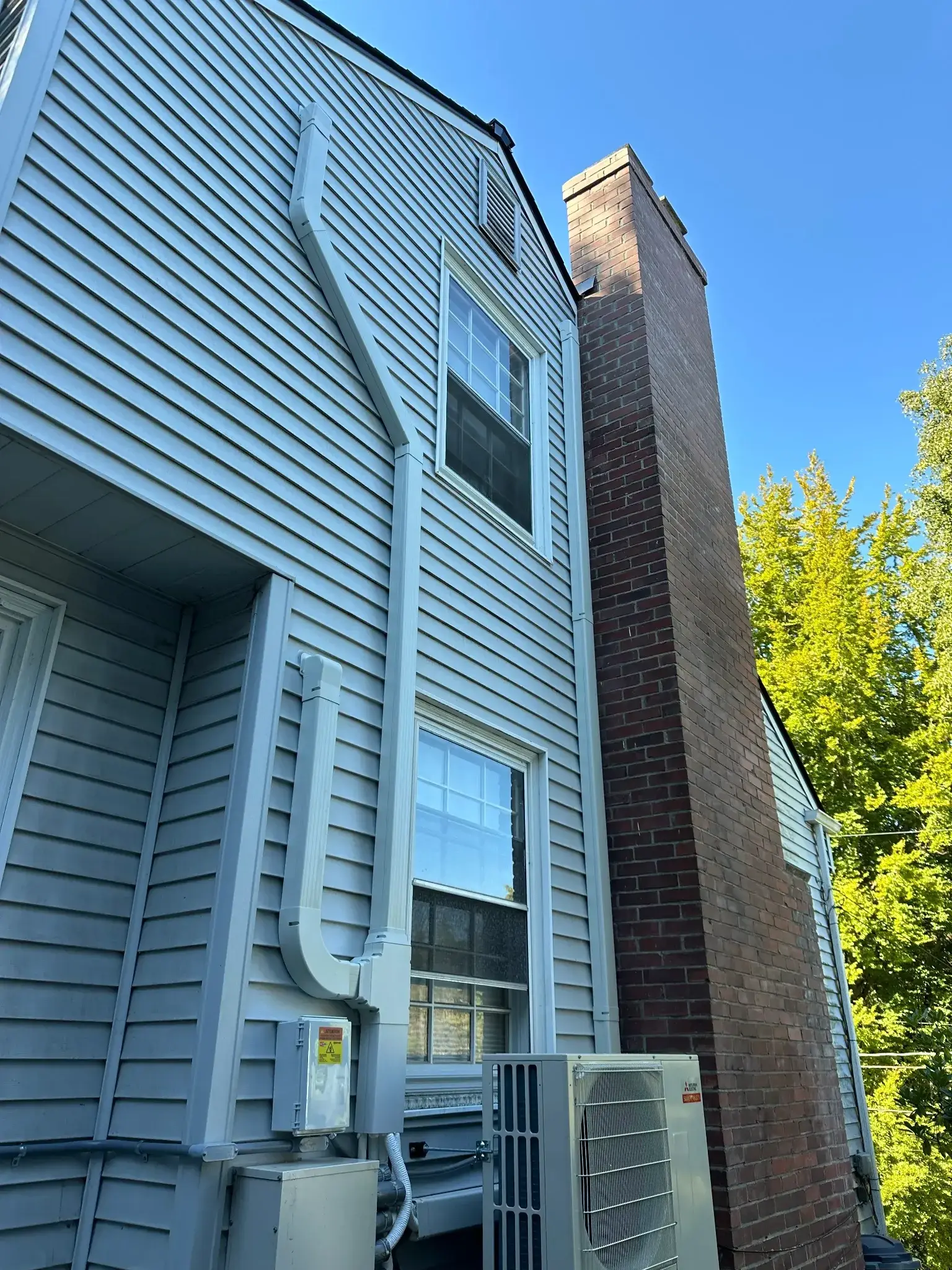 Exterior view of a house featuring vinyl siding, a chimney, and an air conditioning unit.
