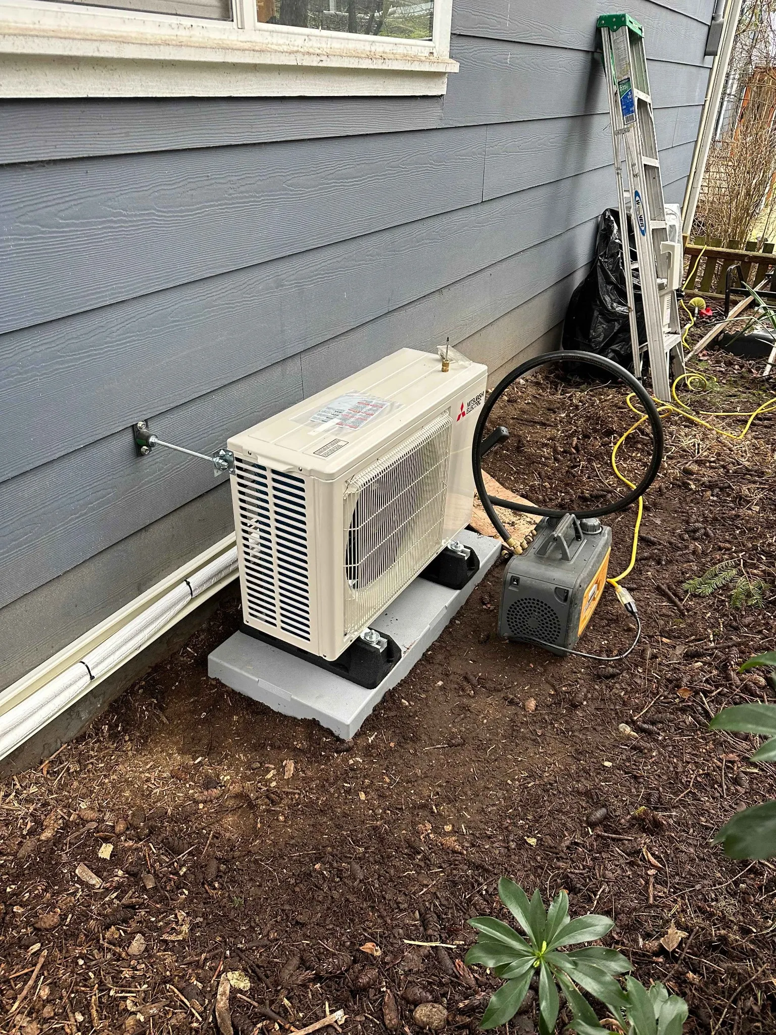 Outdoor air conditioning unit installation next to the house, with a ladder and surrounding landscaping.
