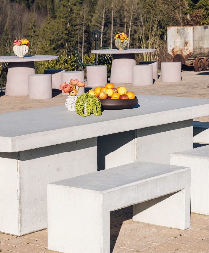 Outdoor concrete table with bench, decorated with fruit bowl and floral arrangements in vases.
