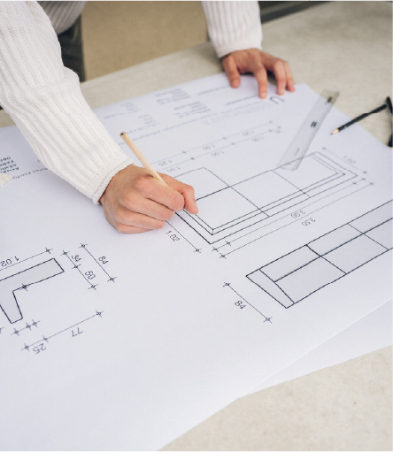 Person drawing on architectural blueprint with ruler and pencil on a table.