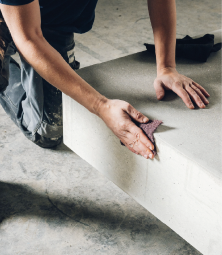 Person kneeling and smoothing concrete surface with a sanding sponge on a construction site.