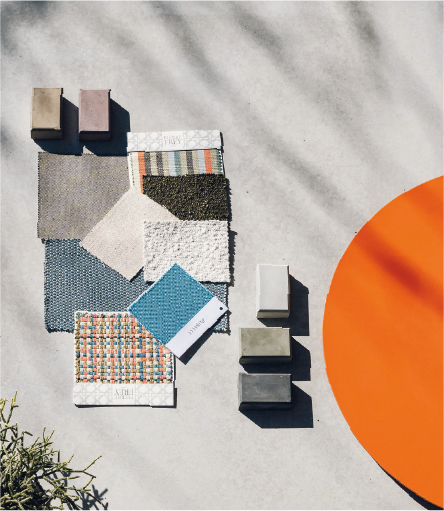 Various fabric swatches and small colored bricks arranged on a concrete floor next to a large orange circle.