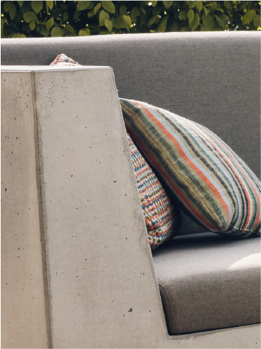 Gray cushioned sofa with two striped decorative pillows partly behind a concrete armrest.