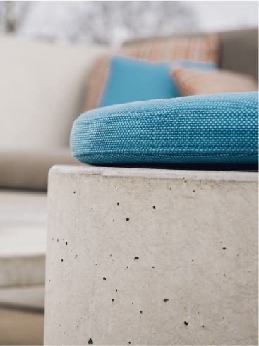Close-up of a blue textured cushion on a concrete surface with blurred outdoor furniture in background.
