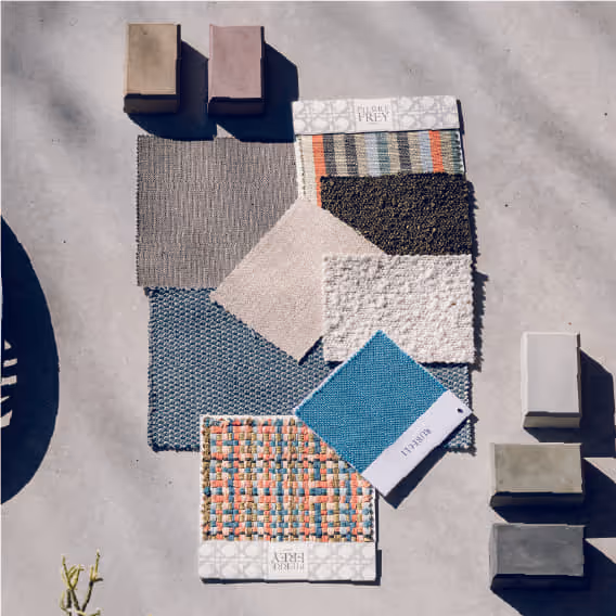 Arranged carpet and fabric swatches in various colors and textures on concrete floor with color blocks.