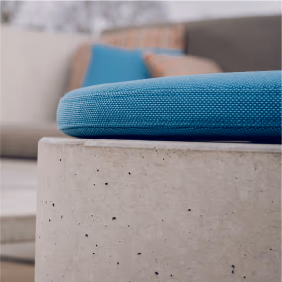 Close-up of a blue fabric cushion on a textured concrete surface with blurred pillows in background.