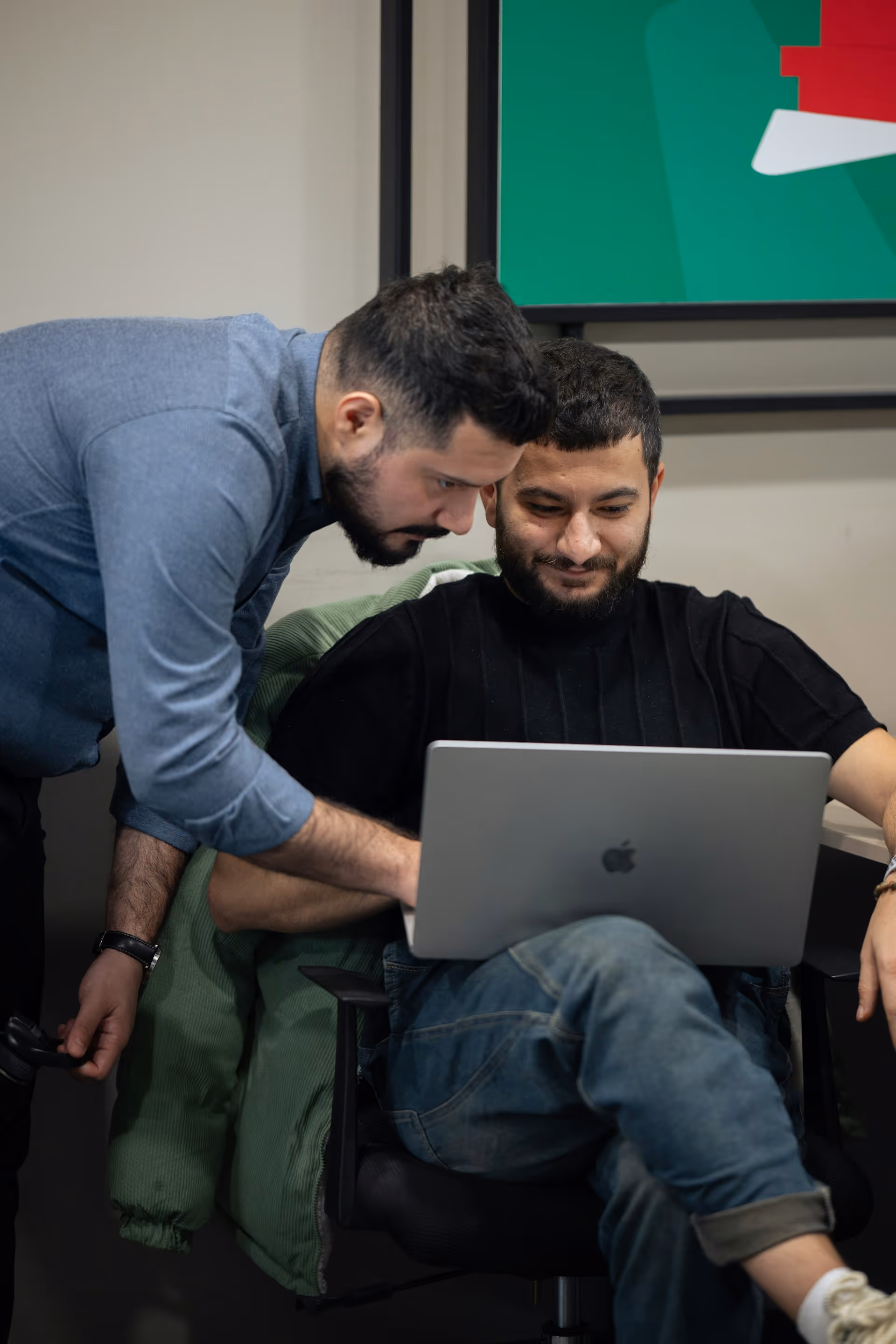 Two men working together on a laptop in an office setting.