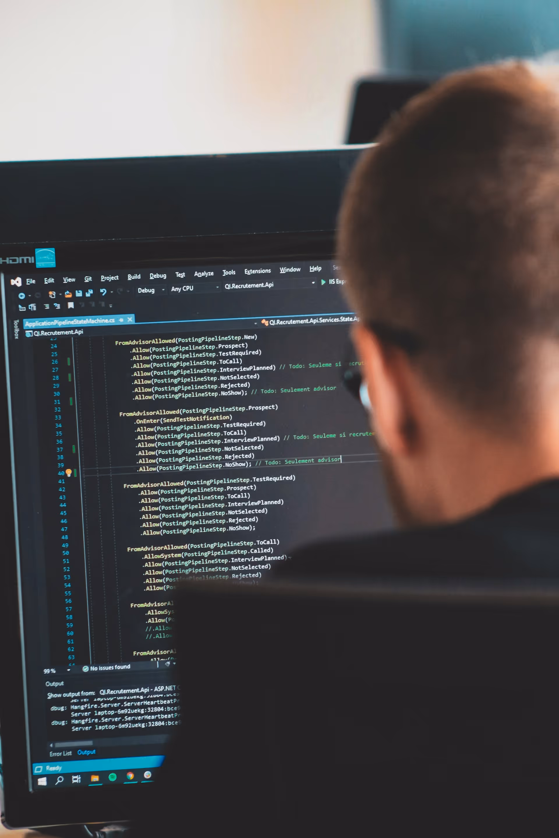 Person wearing glasses looking at computer screen with programming code in a dark-themed editor.