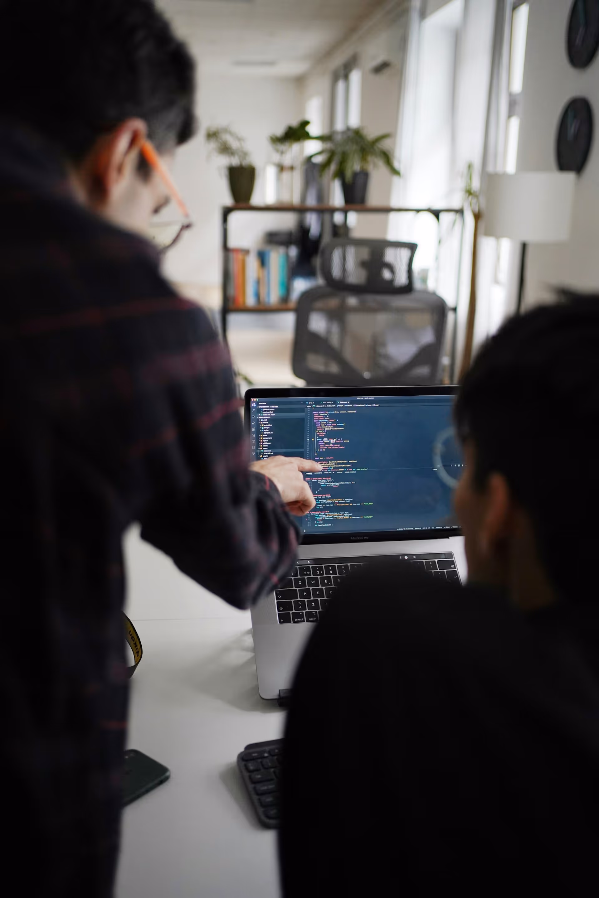 Two people collaborate on coding displayed on a laptop screen in a modern office.