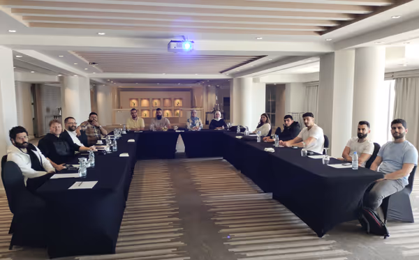 Team of twelve people seated around a U-shaped table in a conference room with a projector on the ceiling.