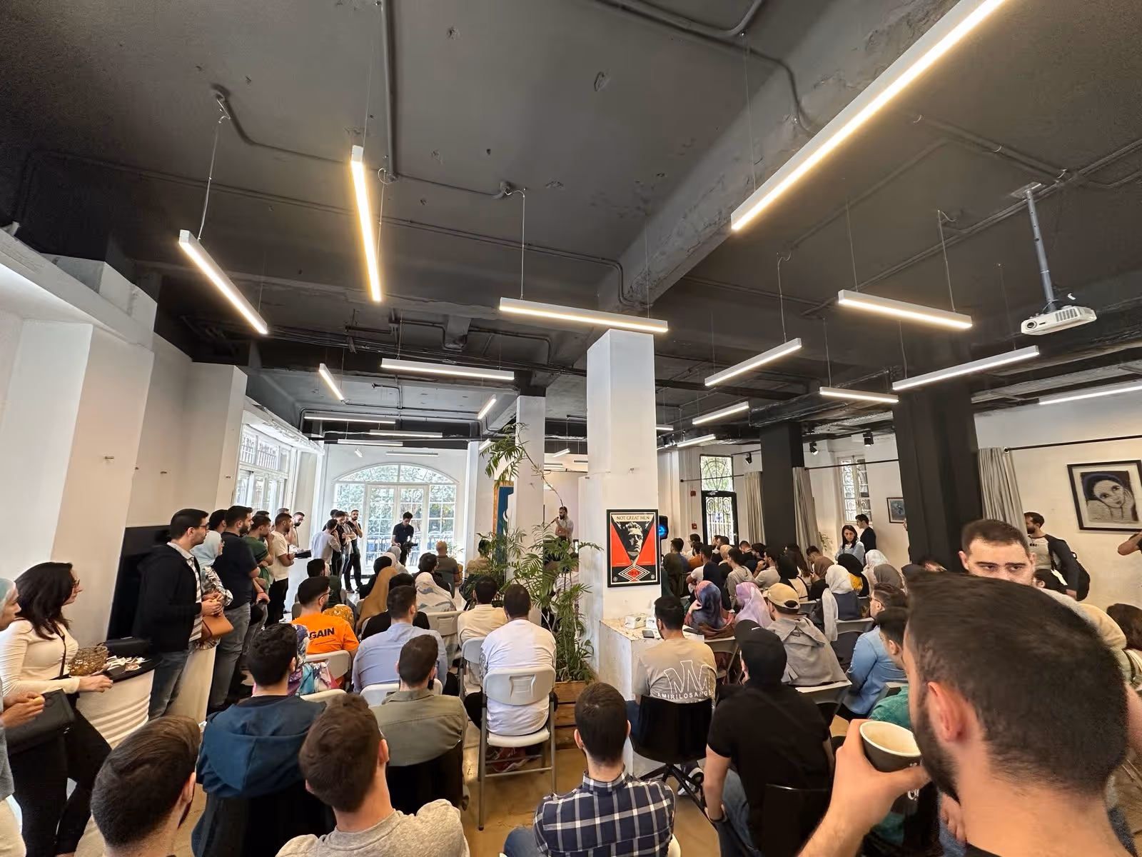 Crowded room with people seated and standing during a presentation or talk in a modern indoor space.