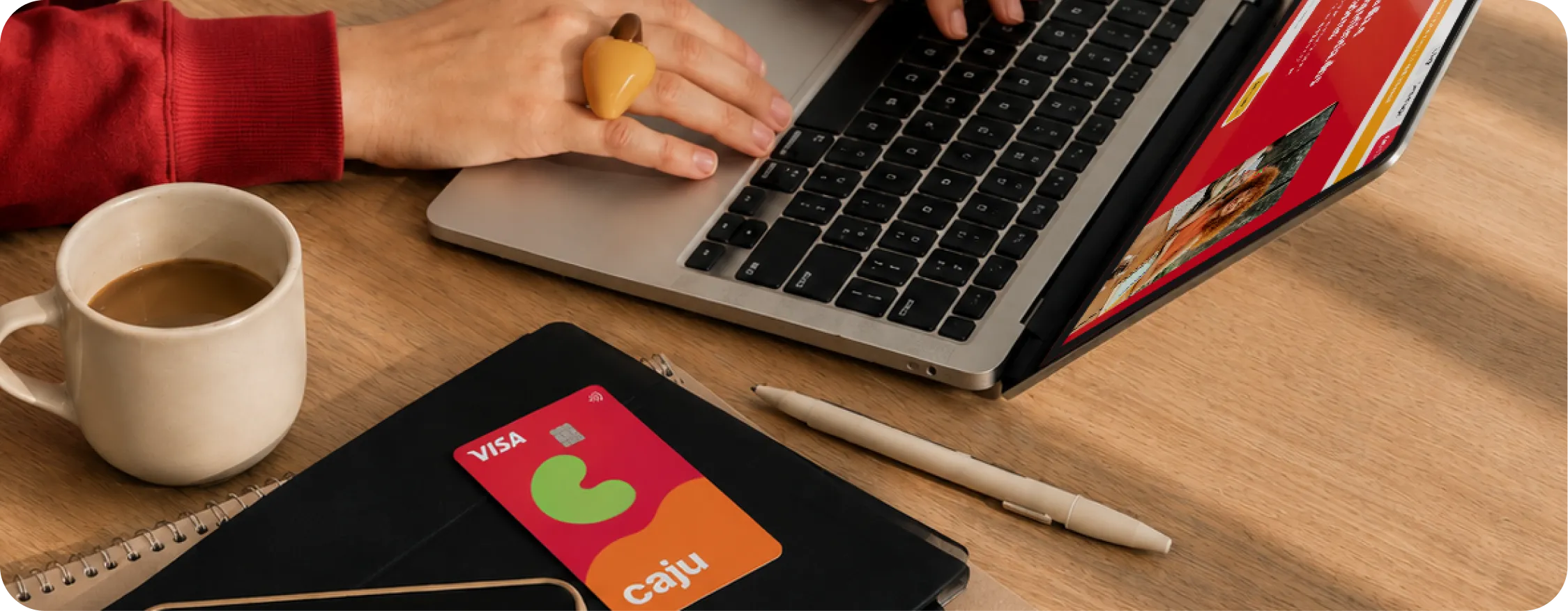 Pessoa usando notebook com o cartão Caju e uma xícara de café sobre a mesa