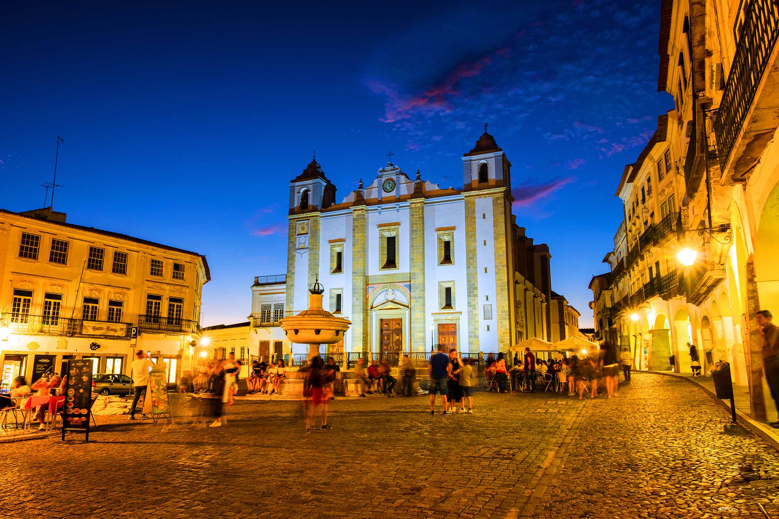 View of Roman Catholic Cathedral of Evora and illuminated historical buildings in the city's square