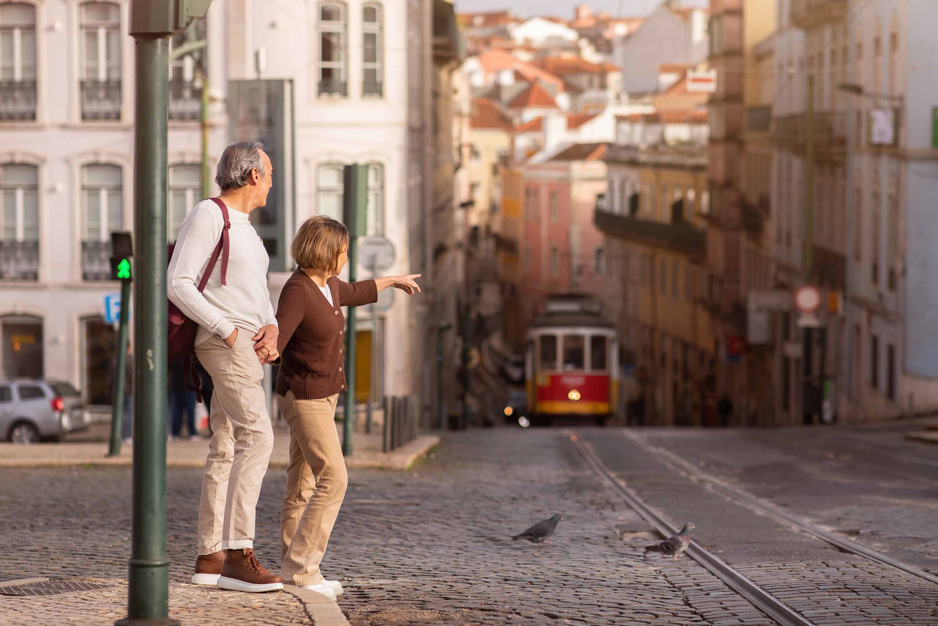 Elderly couple exploring Lisbon, pointing at a famous tram