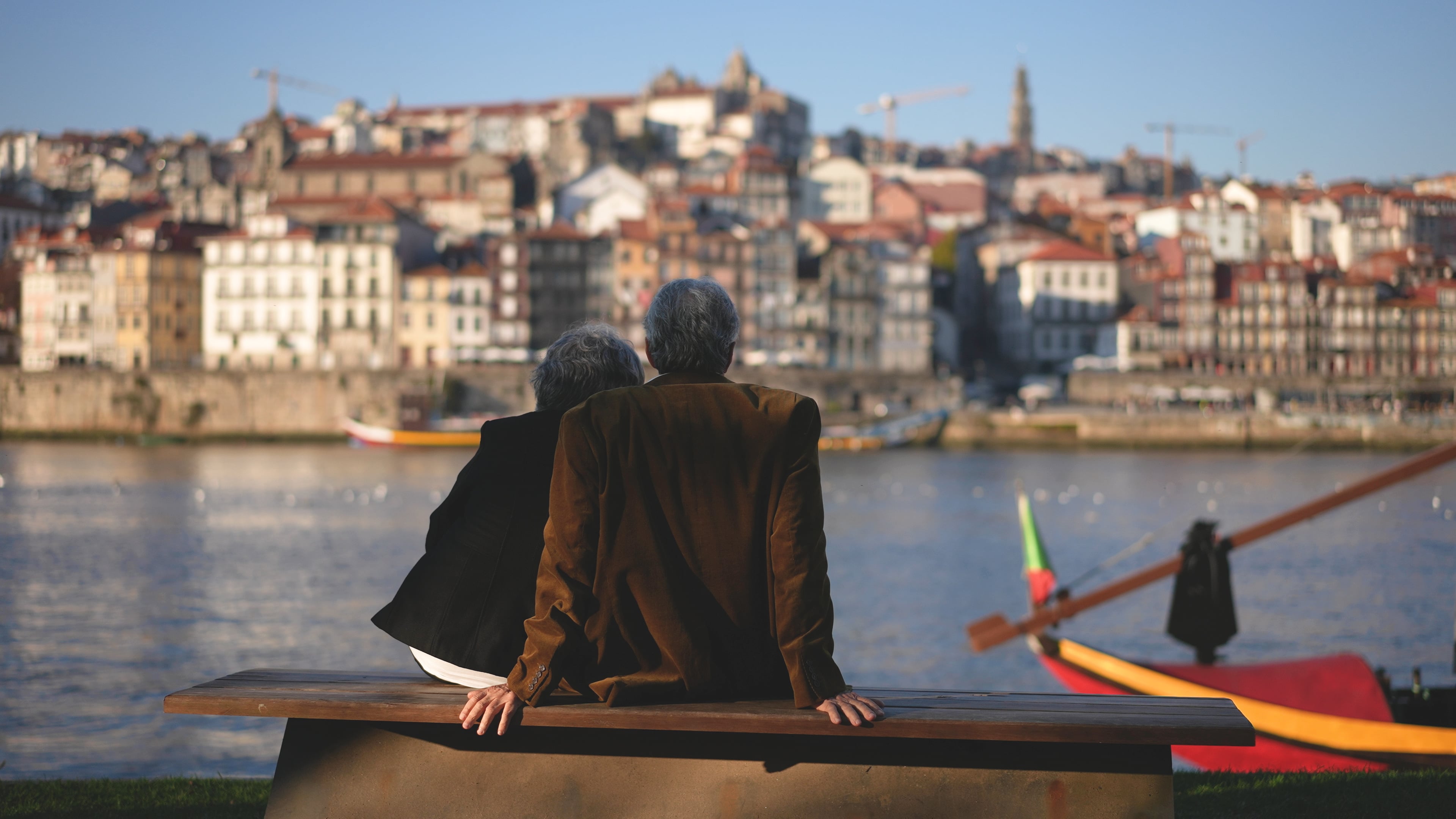Elderly couple sitting by the river, admiring the city of Porto