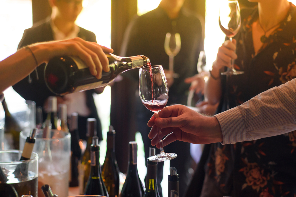 Red wine being poured into a clear glass held by a person at a social gathering