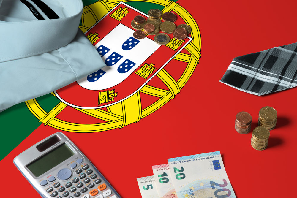 Euro coins and notes with a calculator and a tie resting on the national flag of Portugal
