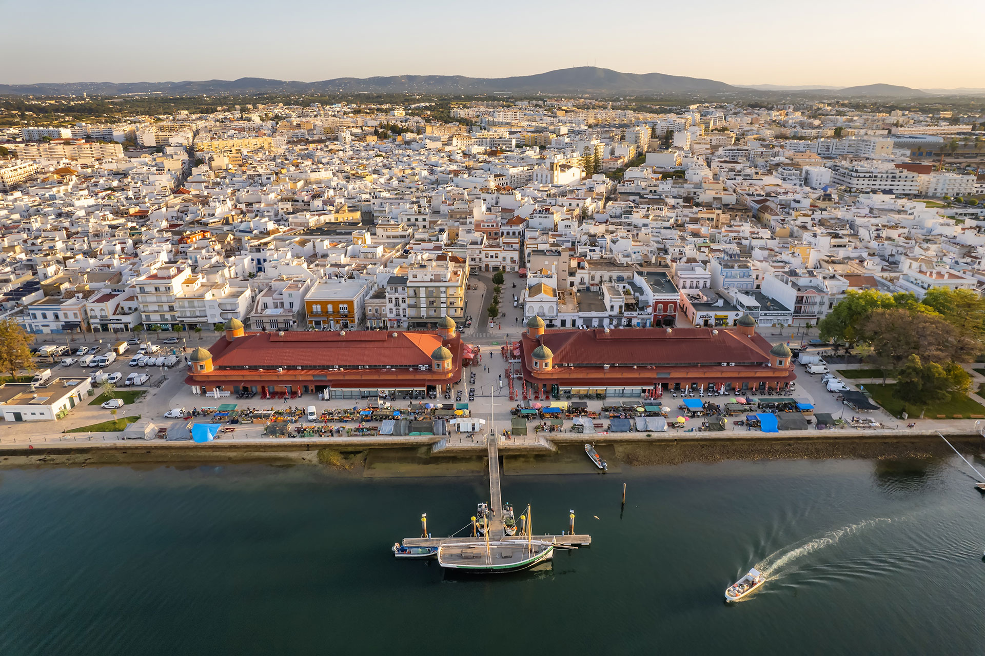 Aerial drone view of the Olhao cityscape with two market buildings by Ria Formosa seaport at sunrise
