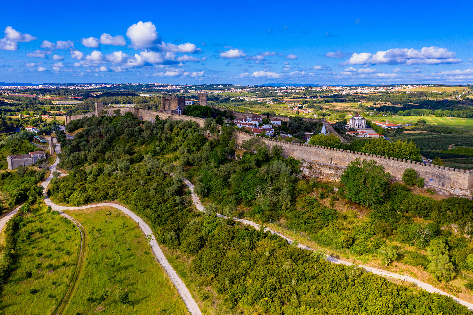 Medieval walls encircle Óbidos’s hilltop homes, with red roofs rising above lush green countryside