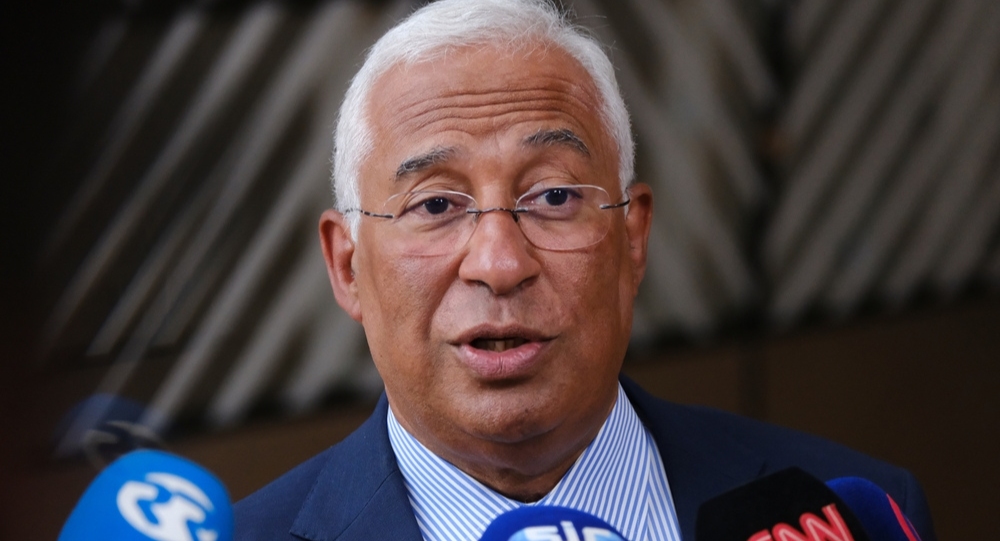 António Costa wearing glasses and blue suit speaking to microphones at a press event