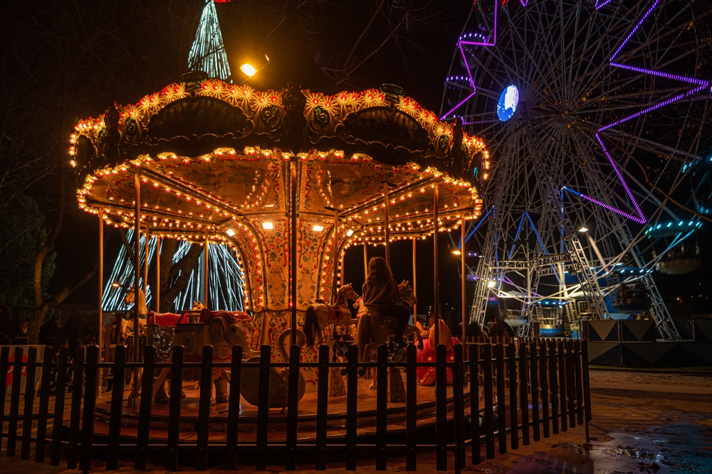 Warmly lit vintage carousel and a purple-lit Ferris wheel at a fairground at night