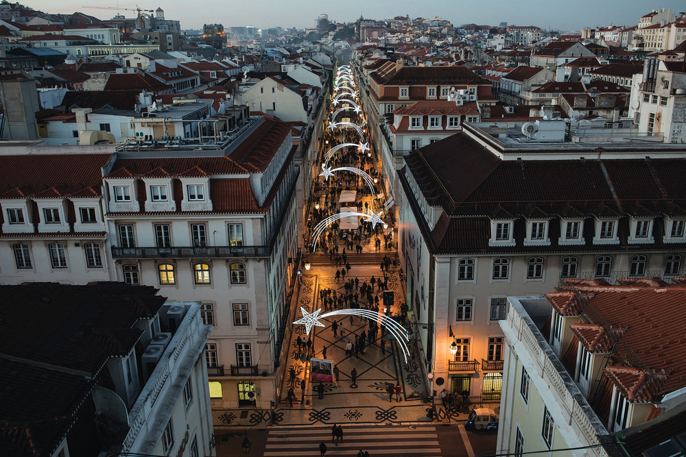 High-angle view of a Lisbon street decorated with shooting star lights between historic buildings