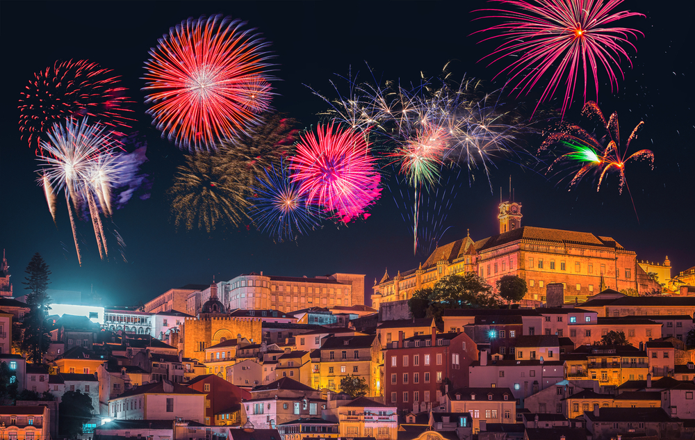 Vibrant red, blue, and gold fireworks burst in the night sky over a historic city hillside