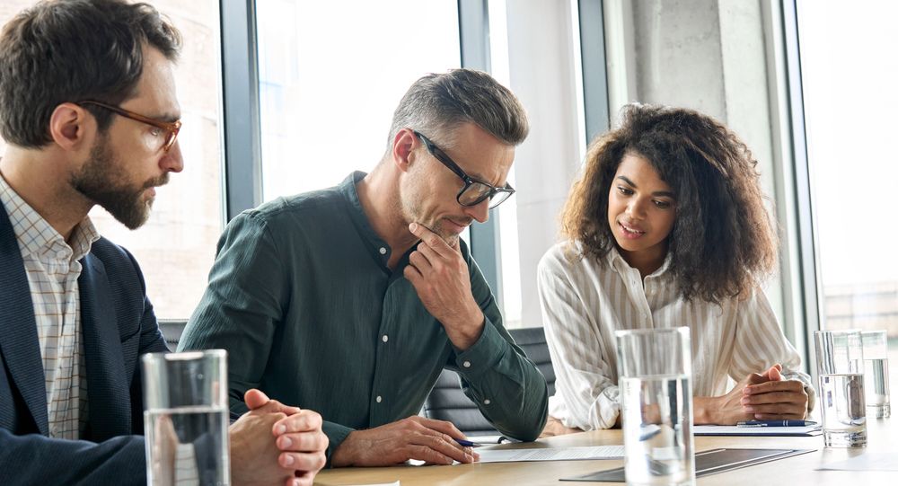 Three professionals reviewing documents and discussing strategy in a bright office setting