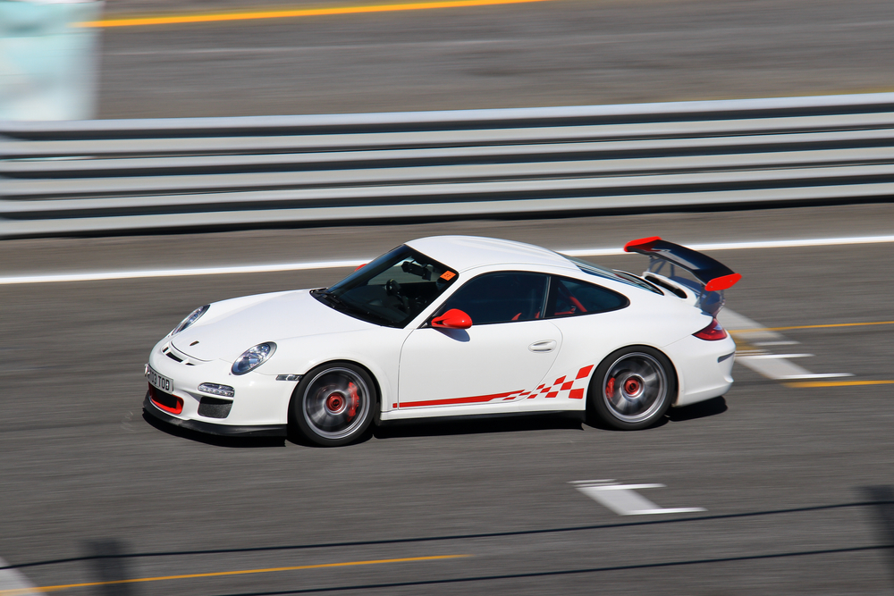 A white Porsche 911 GT3 with red accents speeding around a racetrack with motion blur