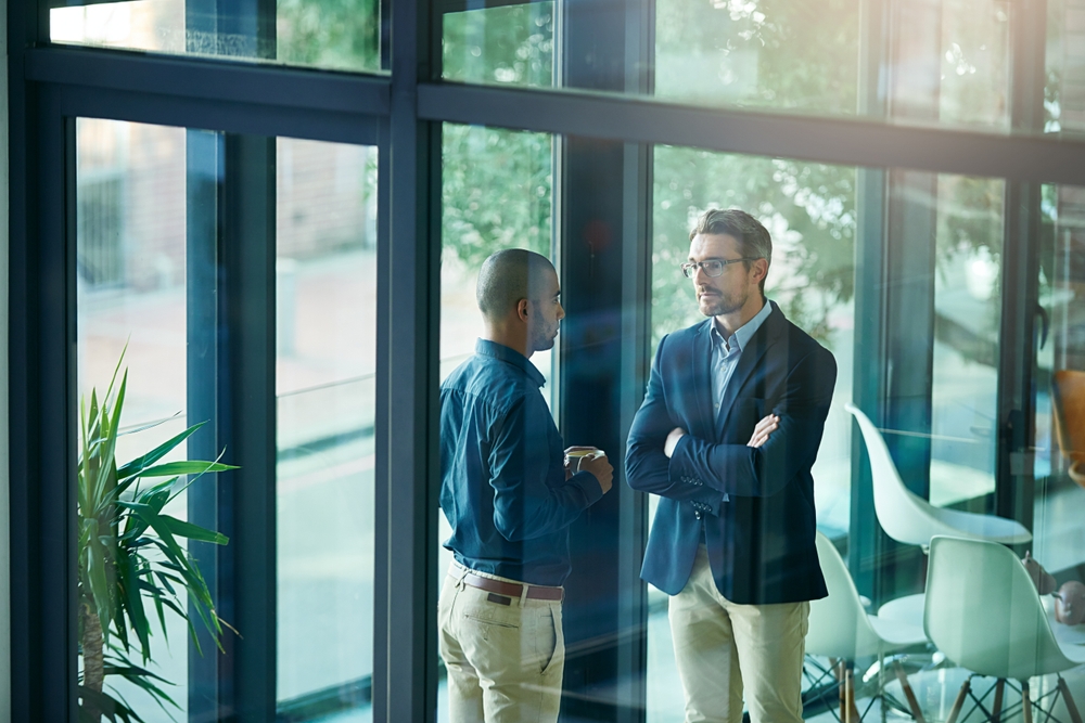 Two businessmen in conversation seen through a glass window in a modern office
