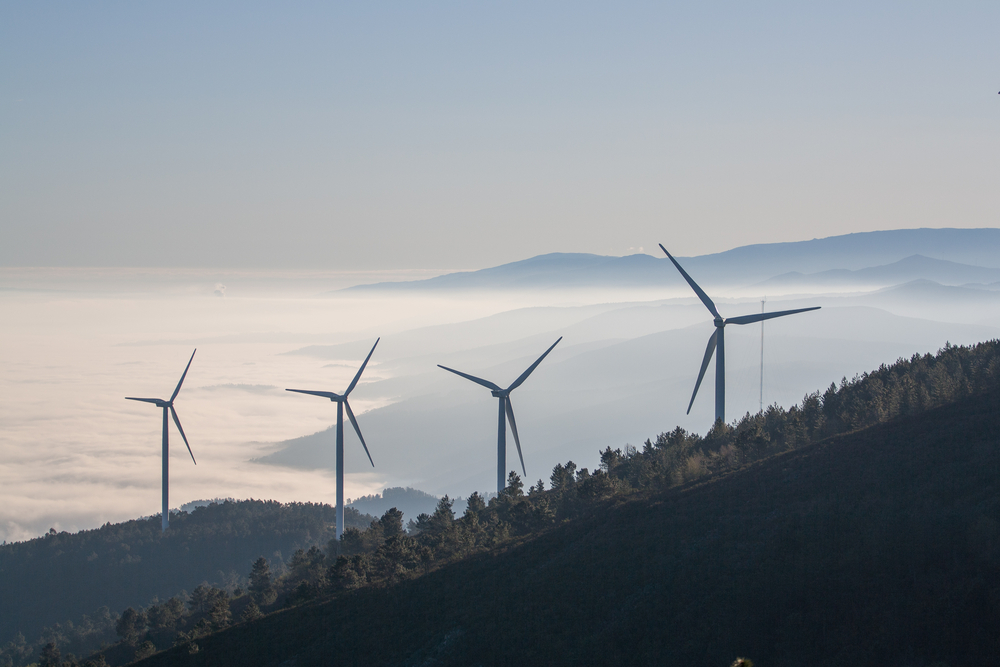 Wind turbines crown Portugal’s misty mountain ridge, blending clean energy with serene natural beauty
