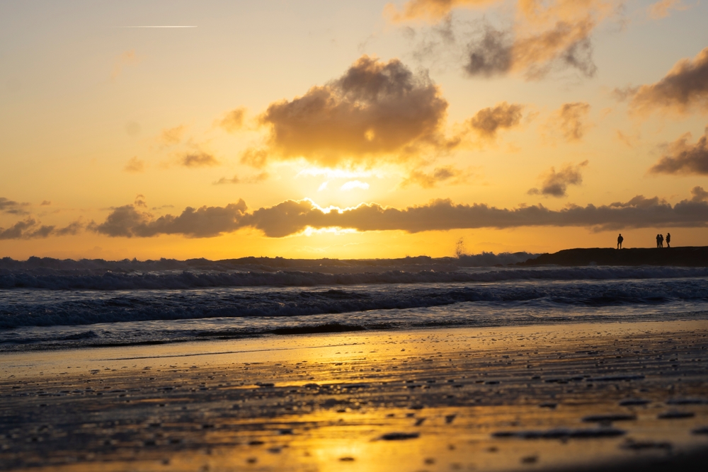 People silhouetted on a rocky shore watching a vibrant orange sunset over the ocean