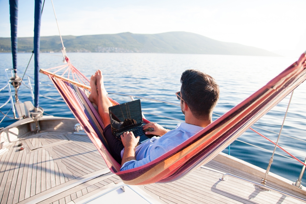 Man with laptop sitting in hammock on the deck of a yacht