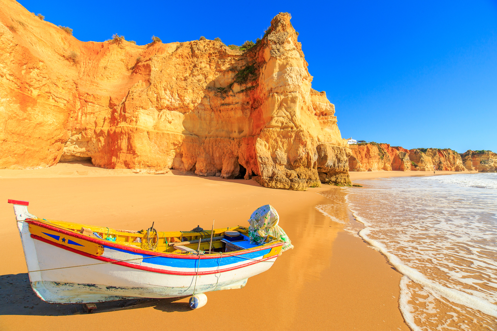 Colorful traditional fishing boat on a golden beach with dramatic orange cliffs in Portugal