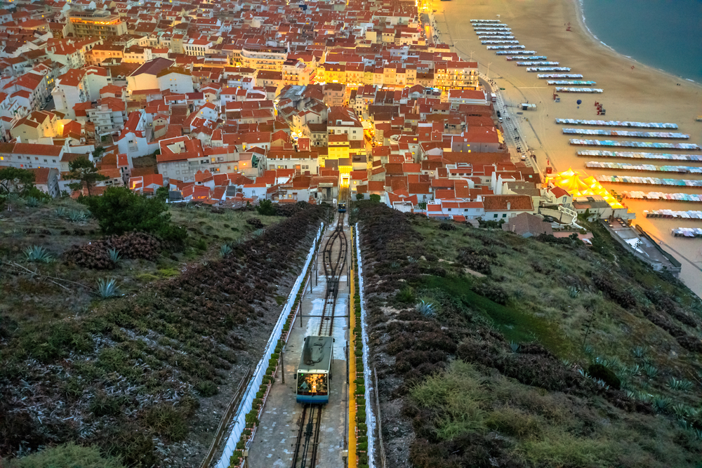 Ascensor da Nazaré funicular descending toward the coastal town and beach at twilight