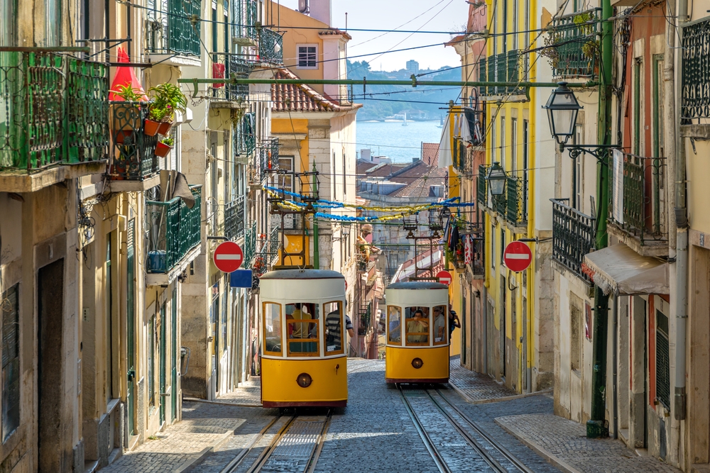 Two yellow funiculars descending a narrow sloped street in Lisbon with a view of the river
