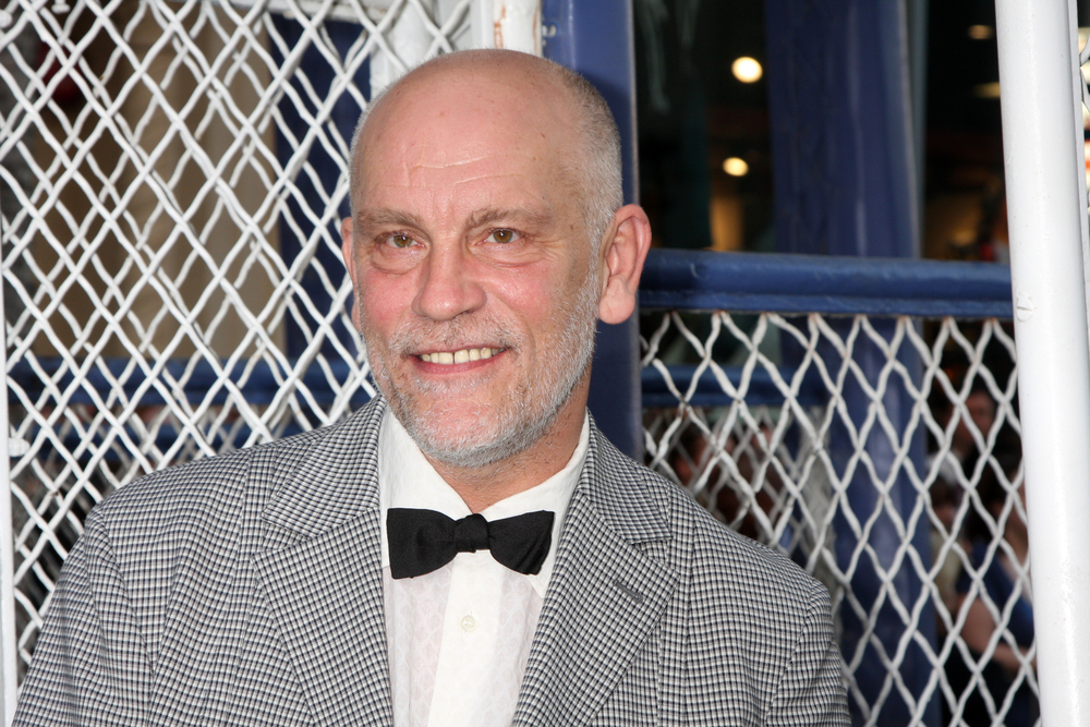 John Malkovich wearing a grey patterned suit and black bow-tie
