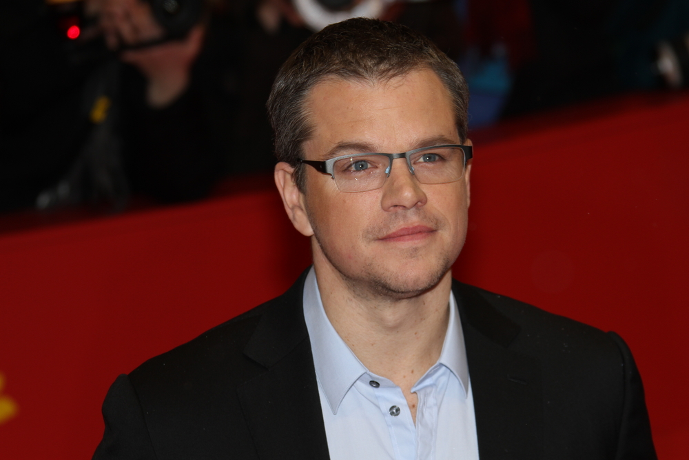 Matt Damon wearing glasses and a black suit jacket on a red carpet
