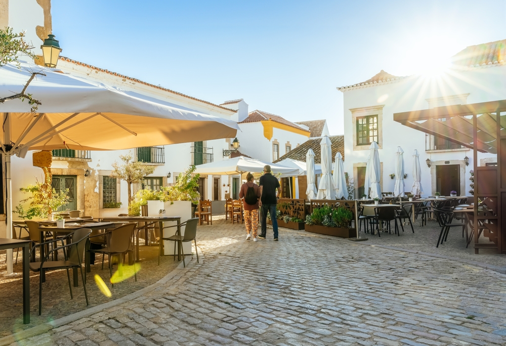 Sunny cobblestone square in Portugal with white buildings and outdoor cafe seating at sunset